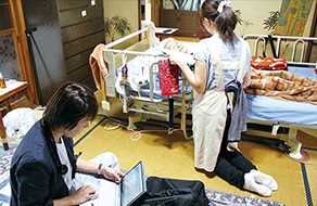訪問先でパソコンに向かう石賀先生と、患者さんに寄り添う看護師さんの画像。